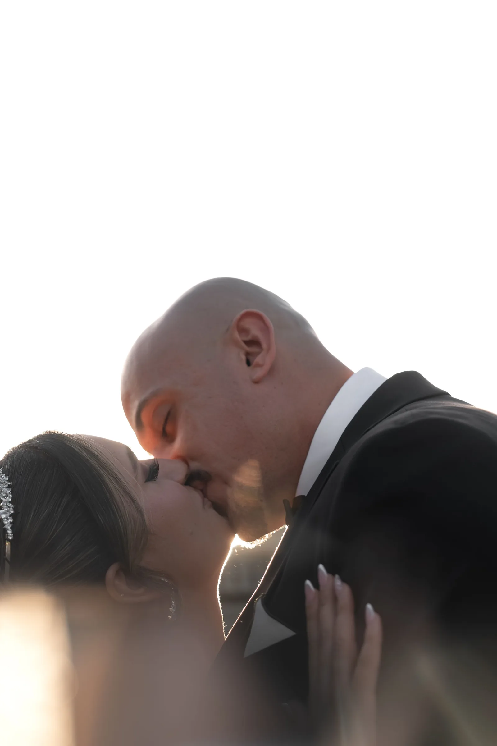 Bride and groom share a first kiss backlit by golden sunlight at their outdoor wedding ceremony.