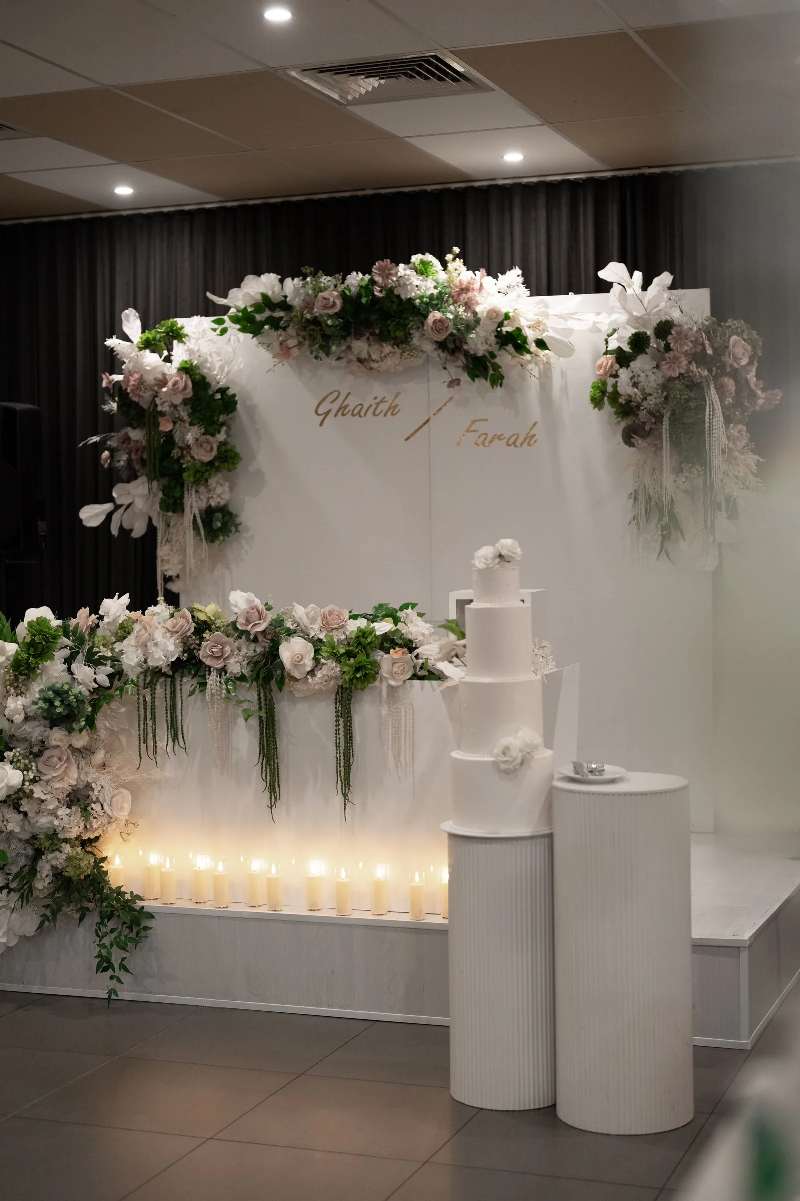Elegant wedding backdrop with white floral arrangements, candles, and a tiered cake for Ghaith and Farah.