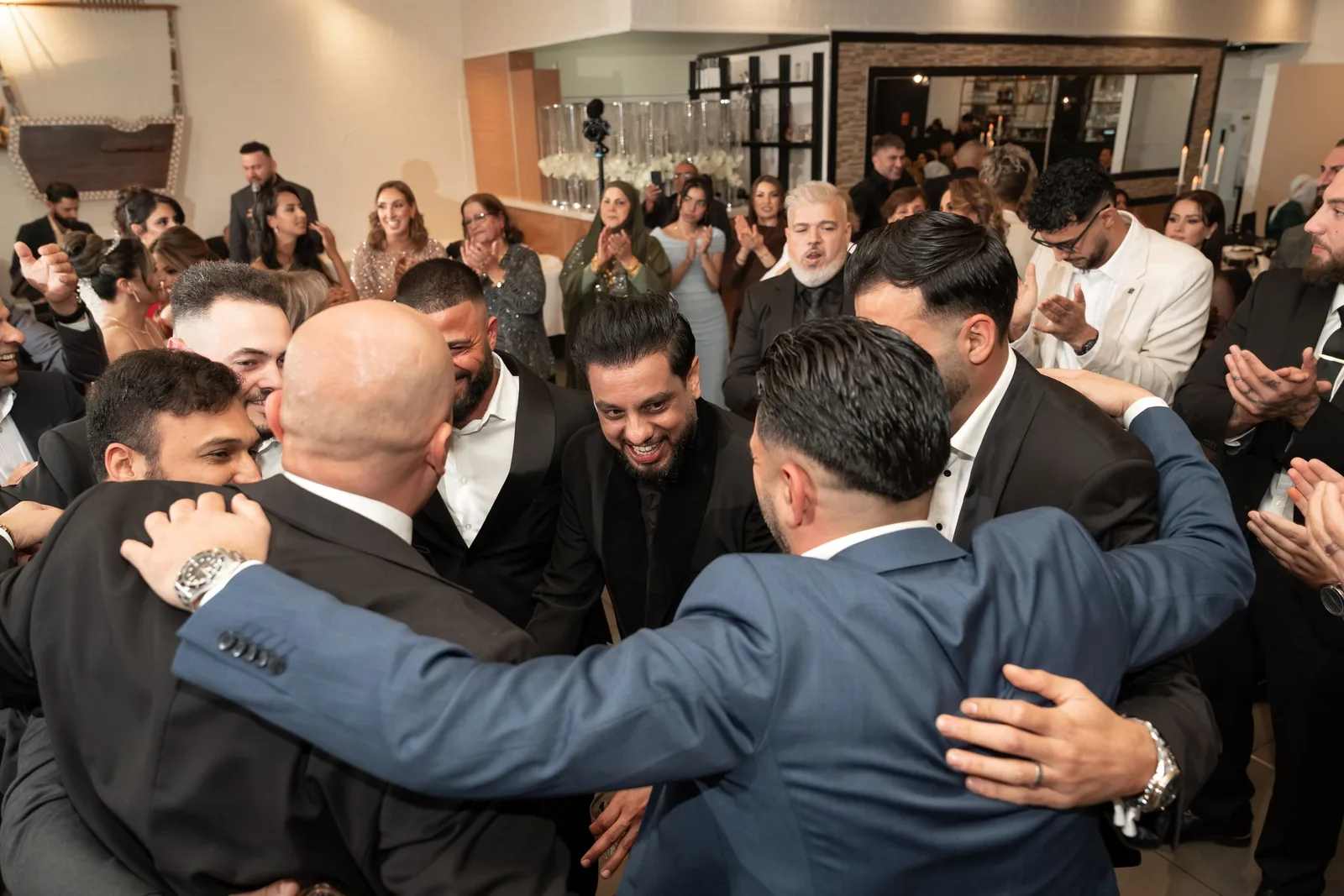 Joyful wedding guests celebrating in a group hug on the dance floor at a lively reception party.