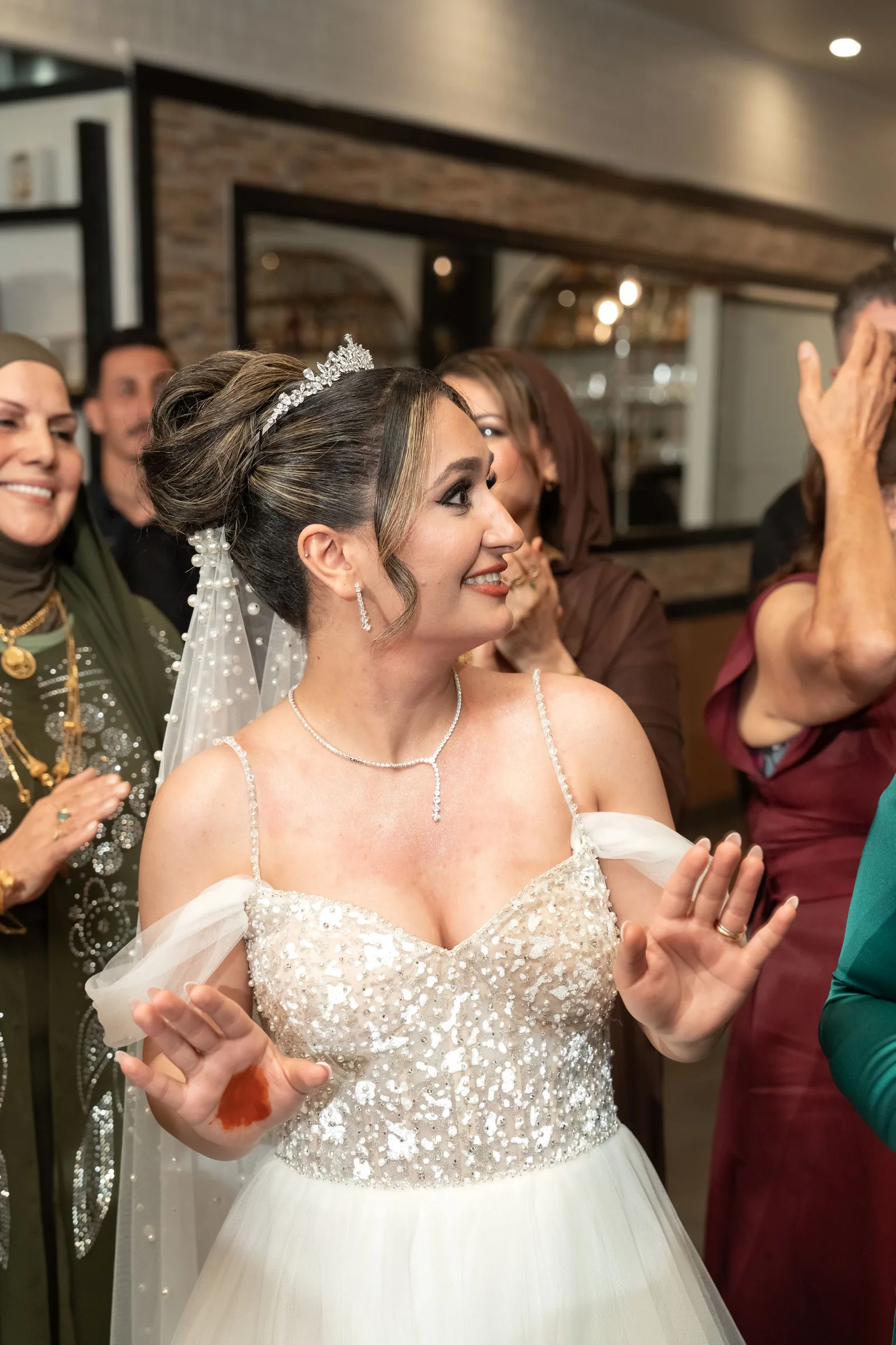 Emotional bride in beaded off-shoulder gown celebrates with guests at wedding reception.