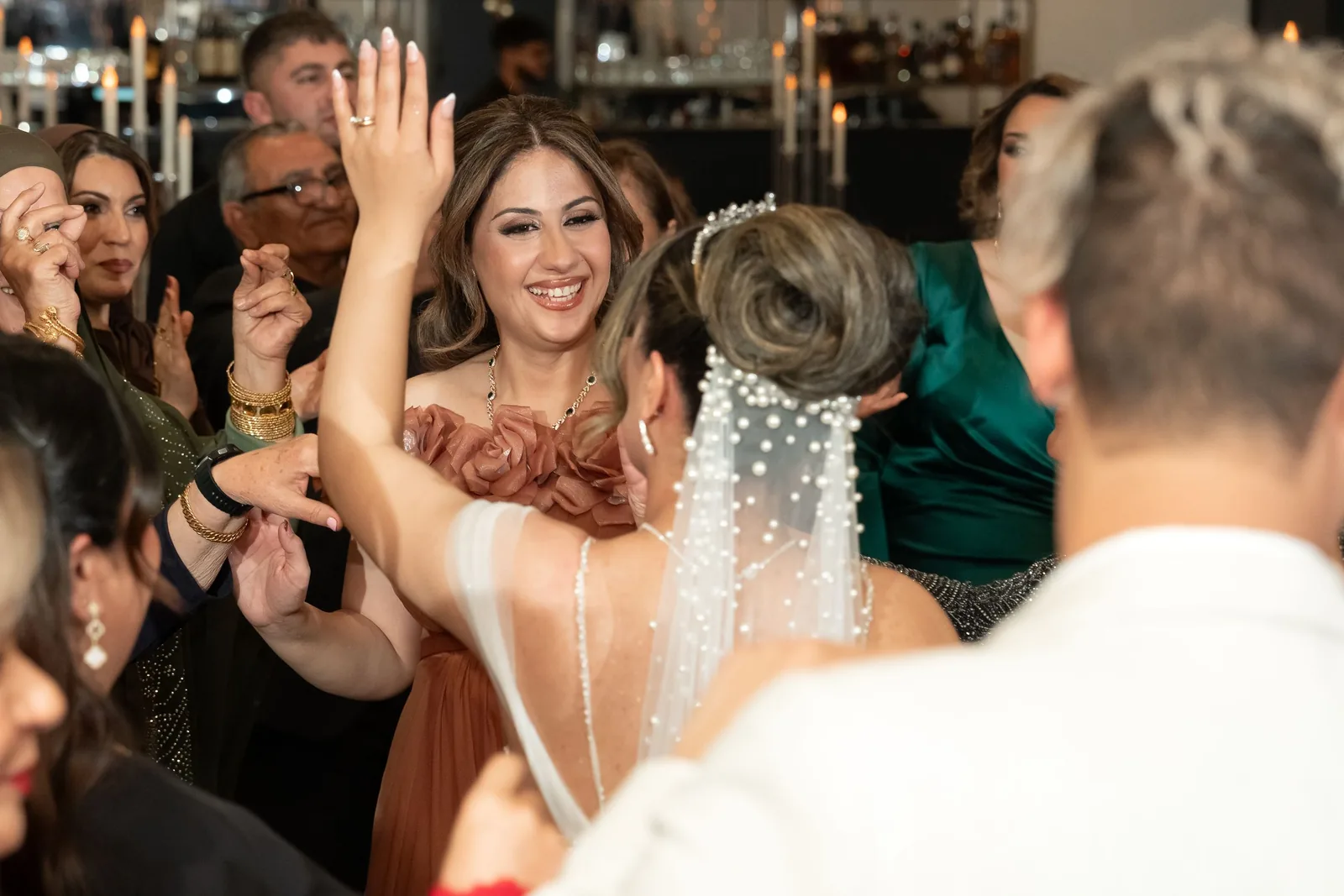 Joyful bride in a pearl-adorned veil dancing and celebrating with guests at her wedding reception.