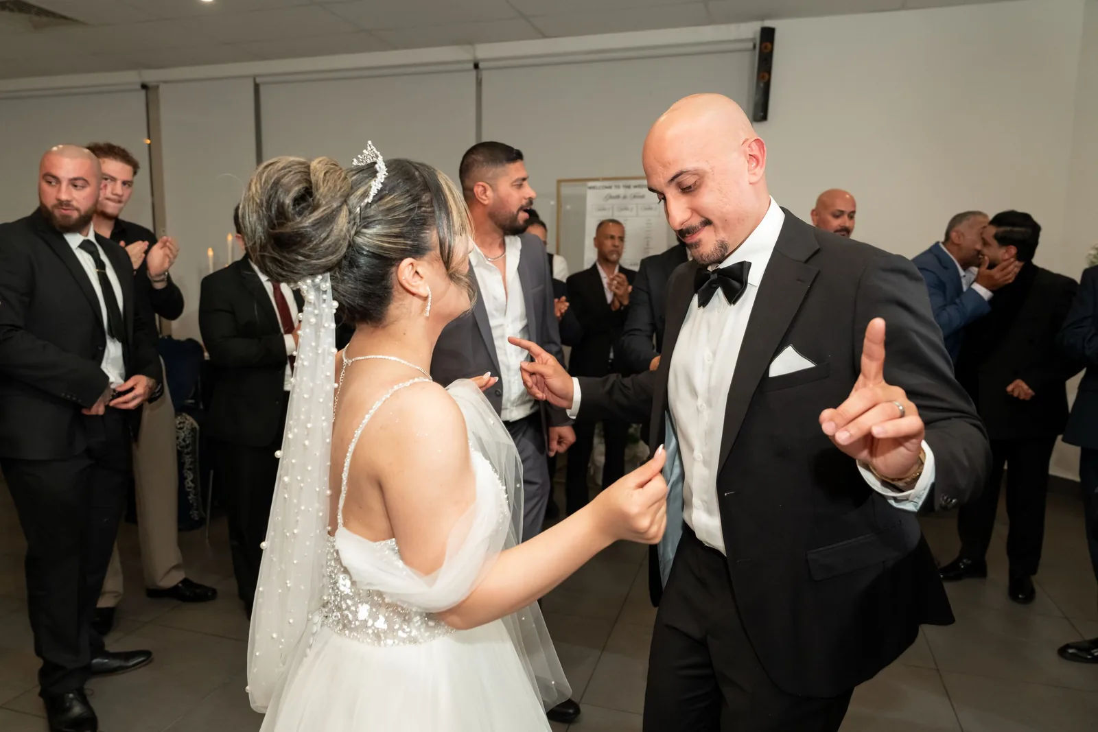 Bride and groom share a dance in elegant wedding attire surrounded by guests at their reception.