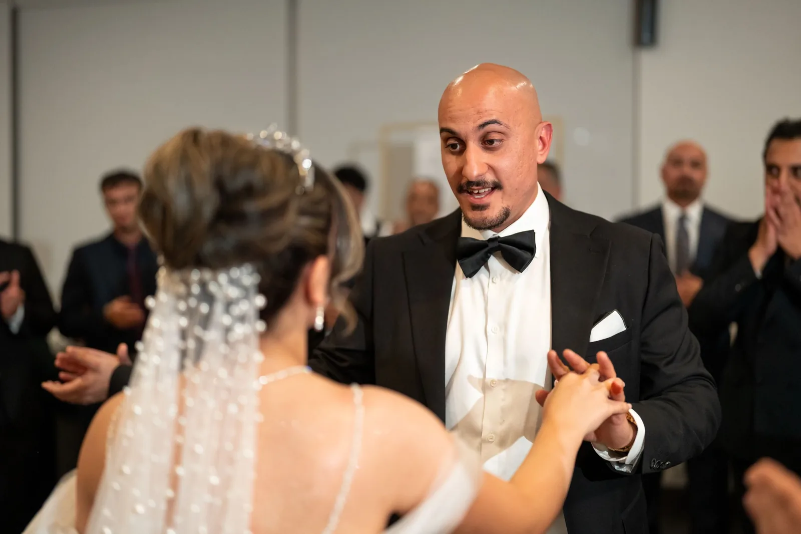 Groom in black tuxedo shares first dance with bride in white gown at elegant wedding reception.