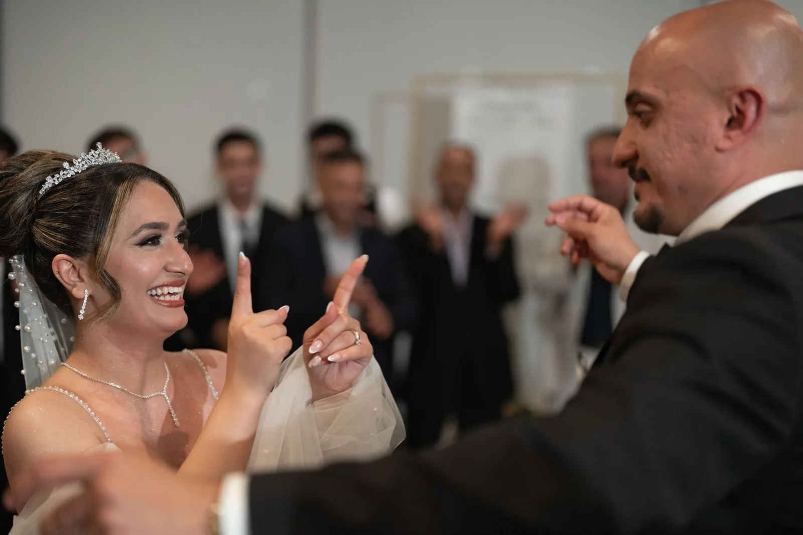 Smiling bride in tiara dances joyfully with groom at lively wedding celebration with guests.