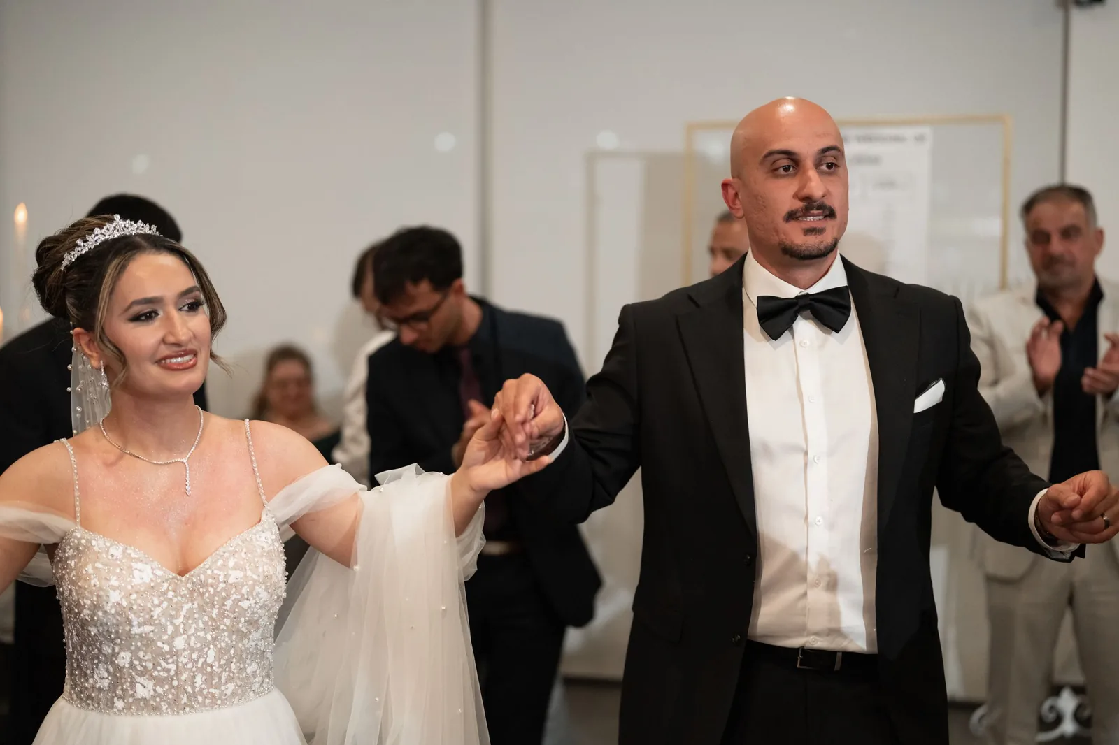 Bride in white gown and groom in tuxedo hold hands while dancing at their wedding reception.
