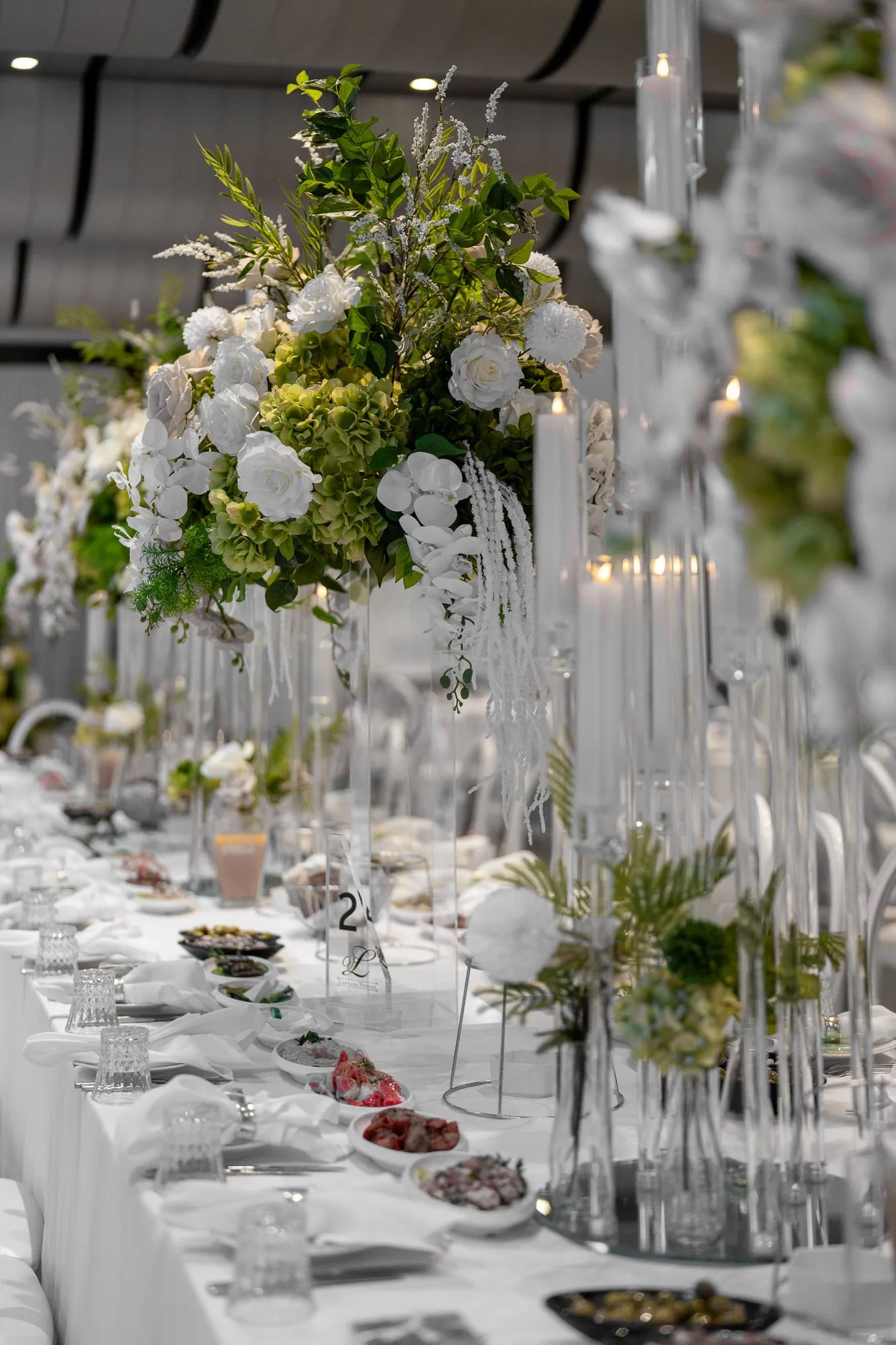 Long banquet tables decorated with white floral centerpieces and crystal vases for an elegant wedding reception.