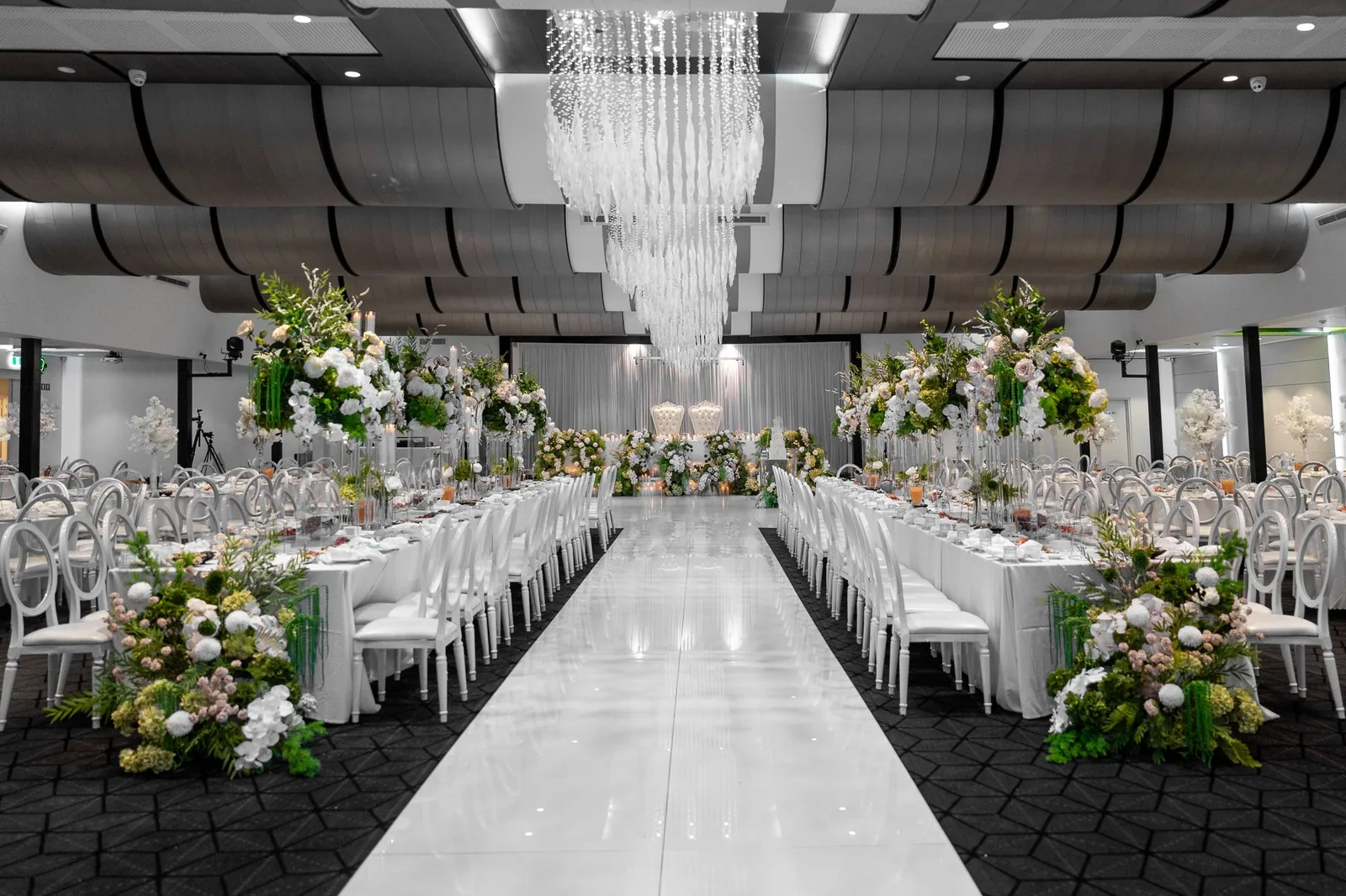 Modern wedding venue with crystal chandeliers and symmetrical table arrangements.