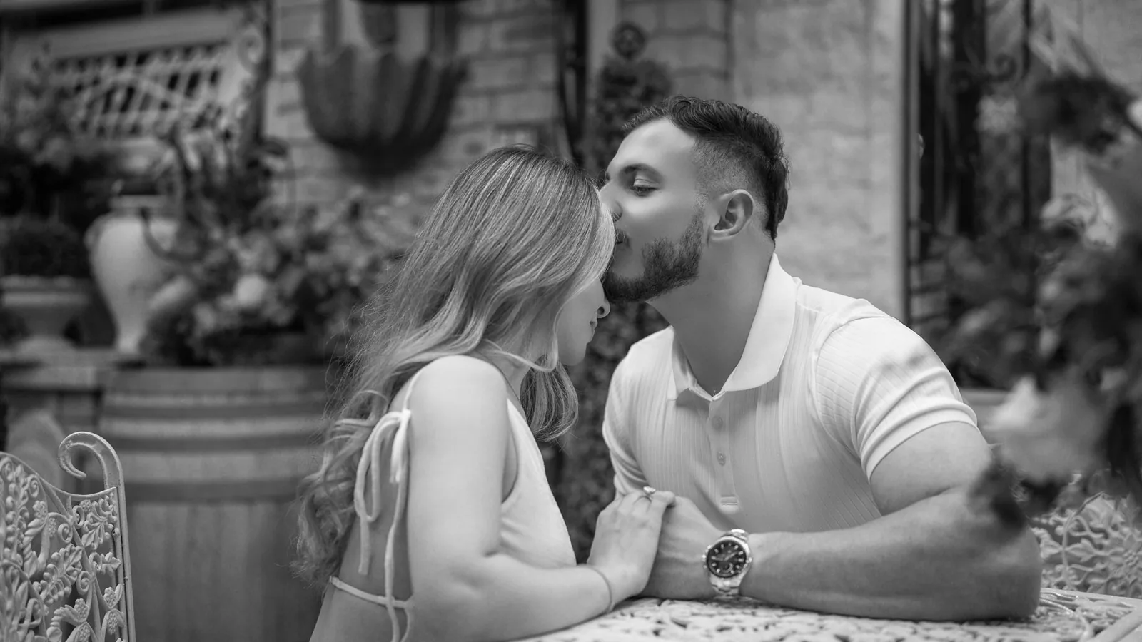 Black and white photo of Manoiel kissing Rita on the forehead at a garden table