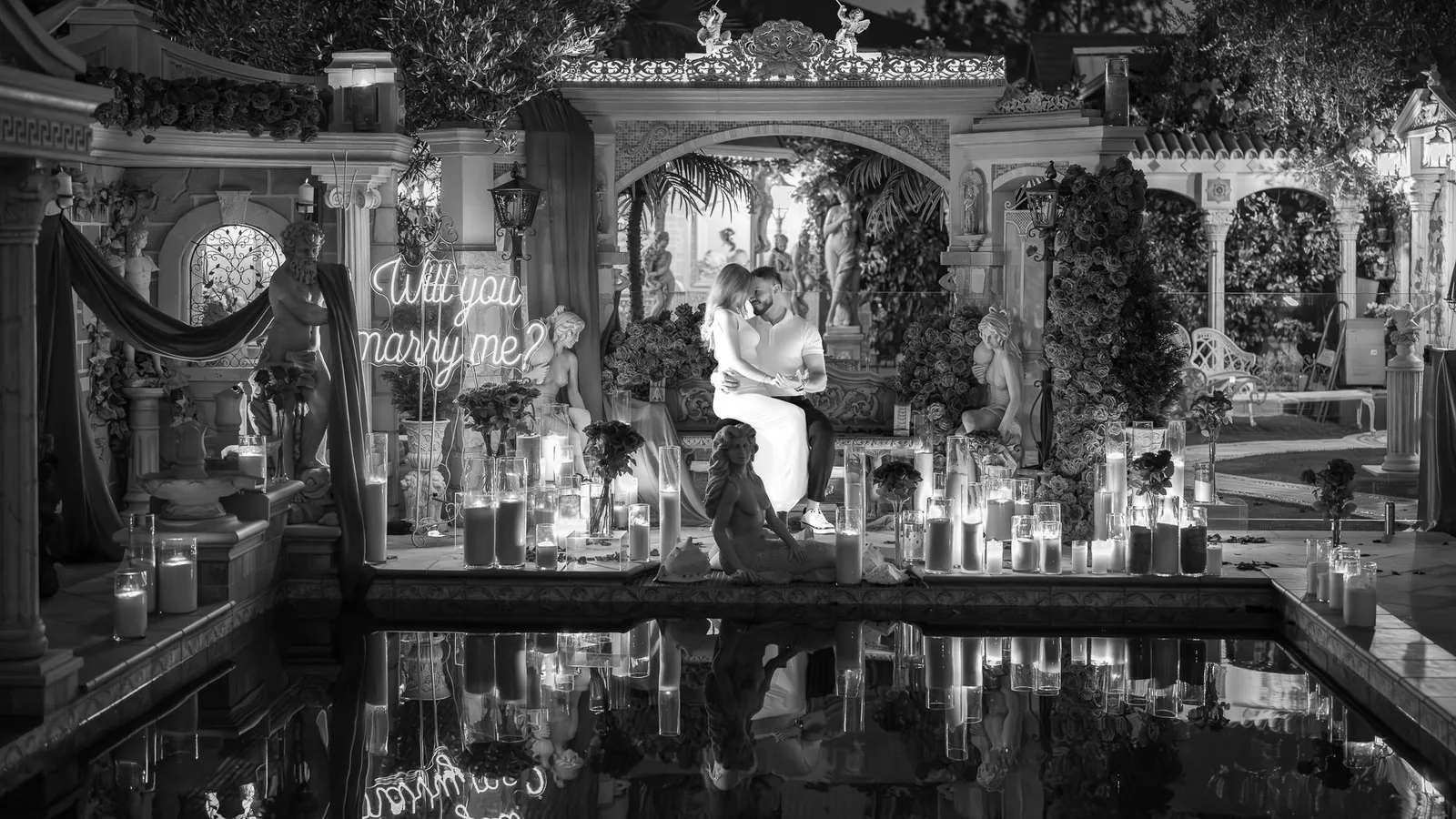 Black and white wide shot of the candlelit proposal courtyard reflected in a still pool
