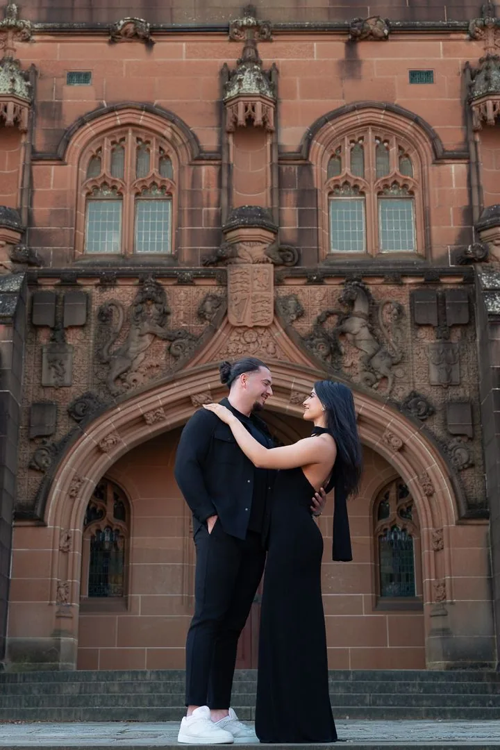 A couple embraces in front of an ornate gothic church facade with detailed stone carvings.