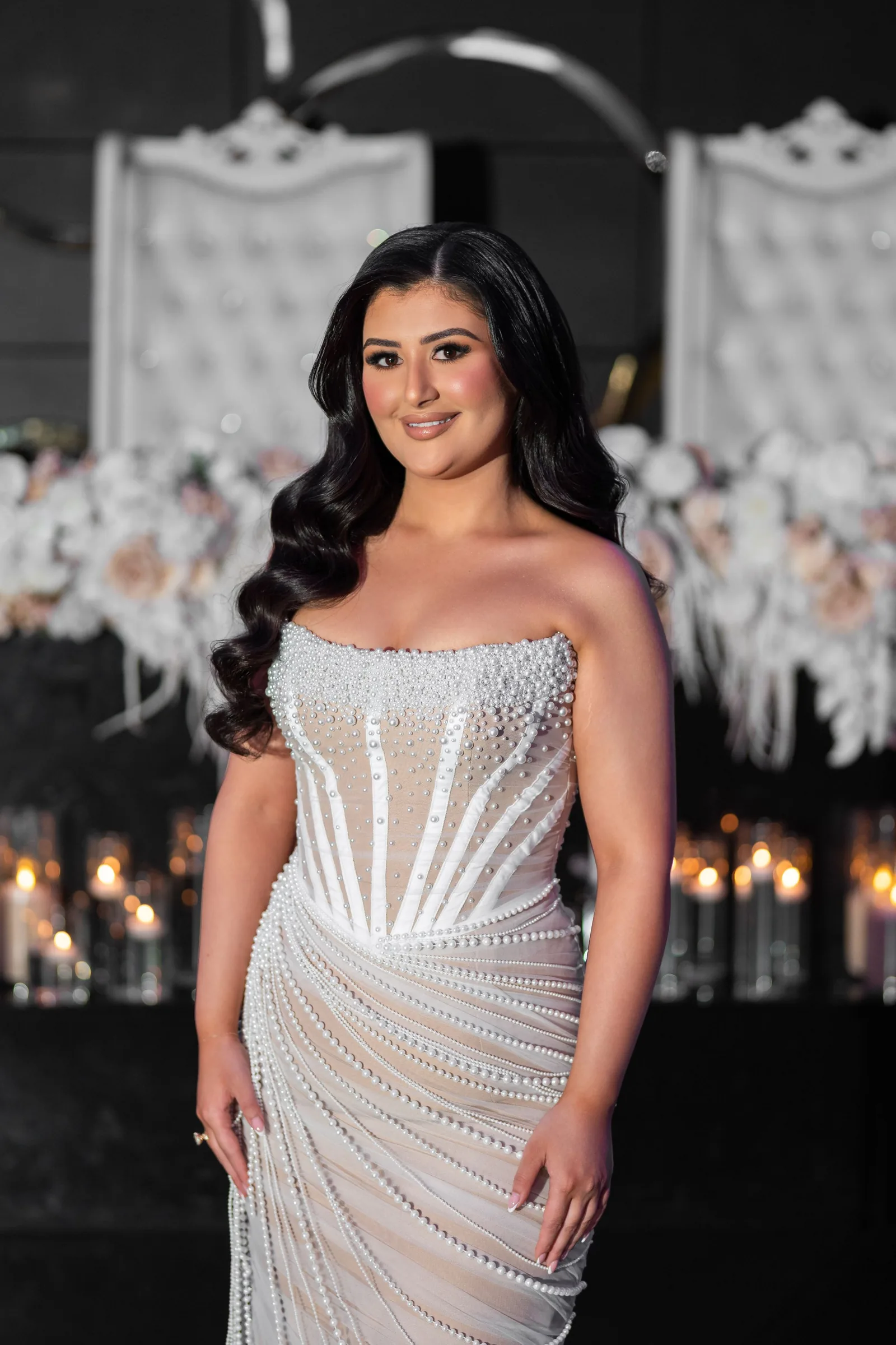 A stunning beaded white wedding gown with corset bodice and sweeping crystal details in an elegant venue with candles.