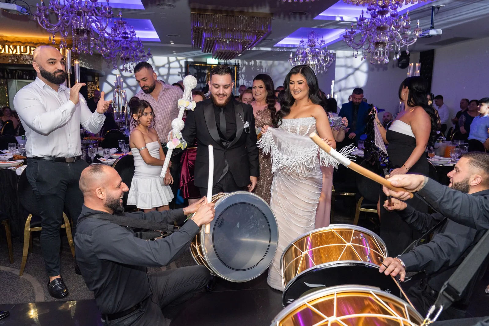 Musicians perform traditional Middle Eastern music with drums and percussion at a wedding reception with purple lighting.