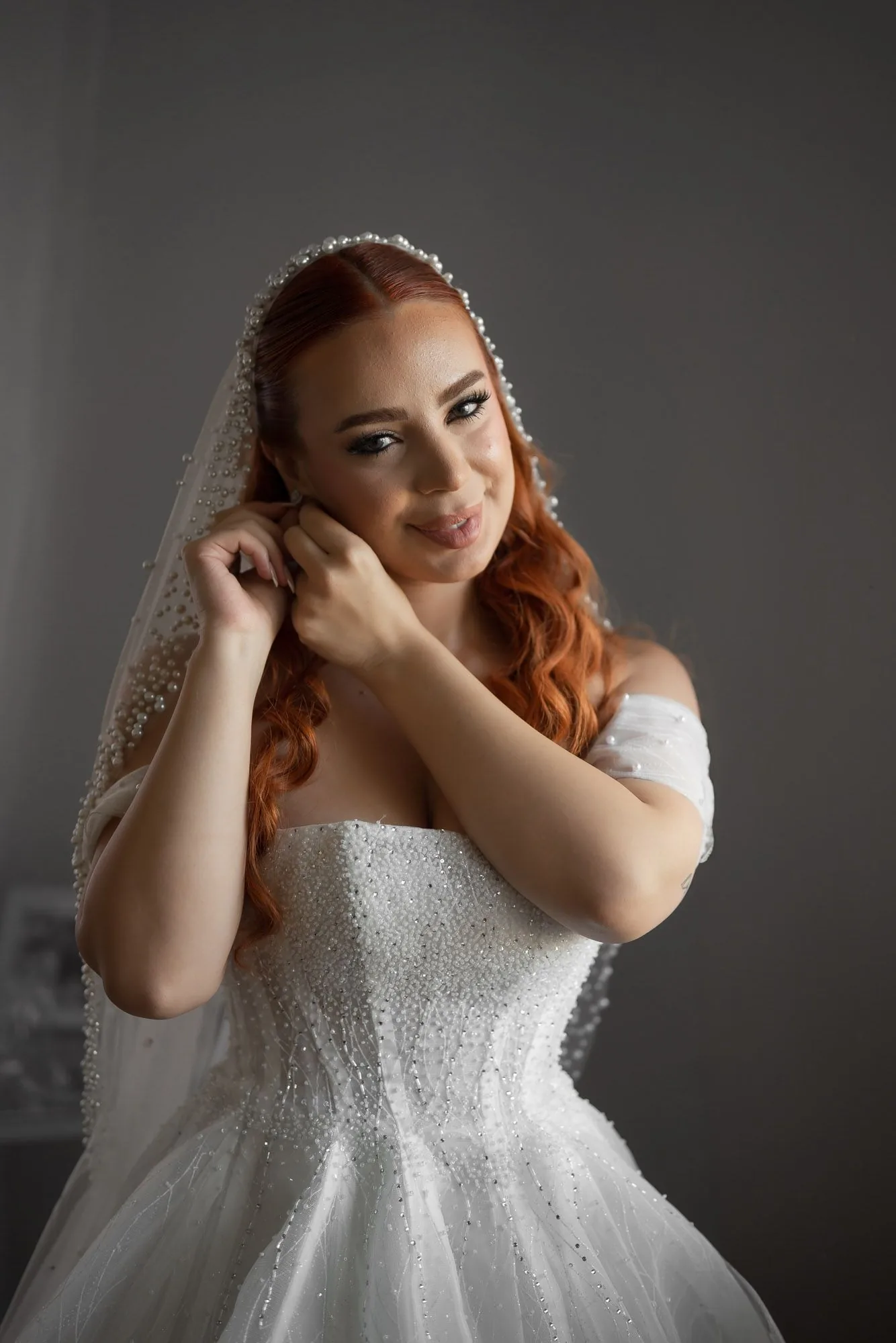 A bride wearing a sparkling white ball gown and veil poses against a dark background.