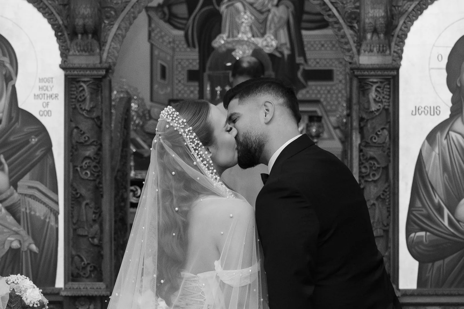Intimate black and white wedding kiss photo captured between religious iconography in church.