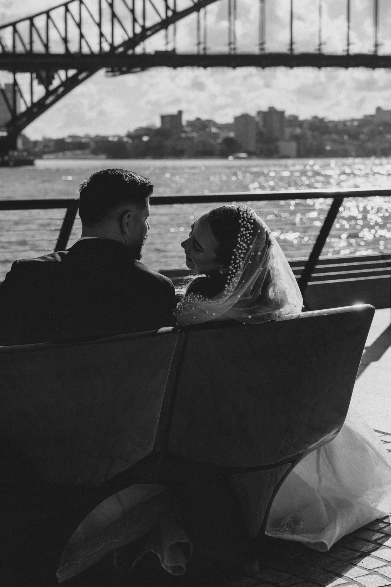 Couple sitting on bench overlooking Sydney Harbour Bridge in romantic wedding photo.