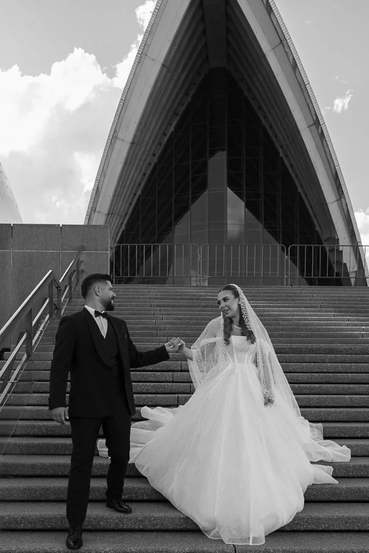 Wedding couple posing on Sydney Opera House steps in elegant formal attire.